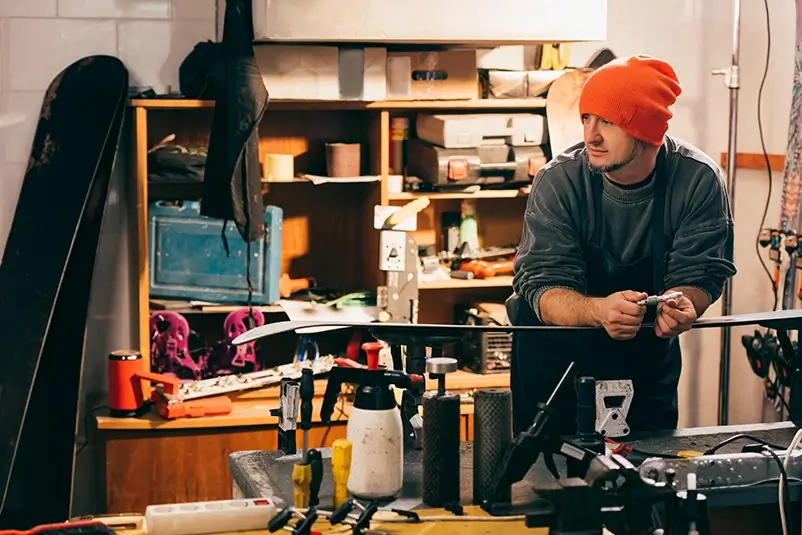 Young adult working on a pair of skis in a snow equipment workshop.
